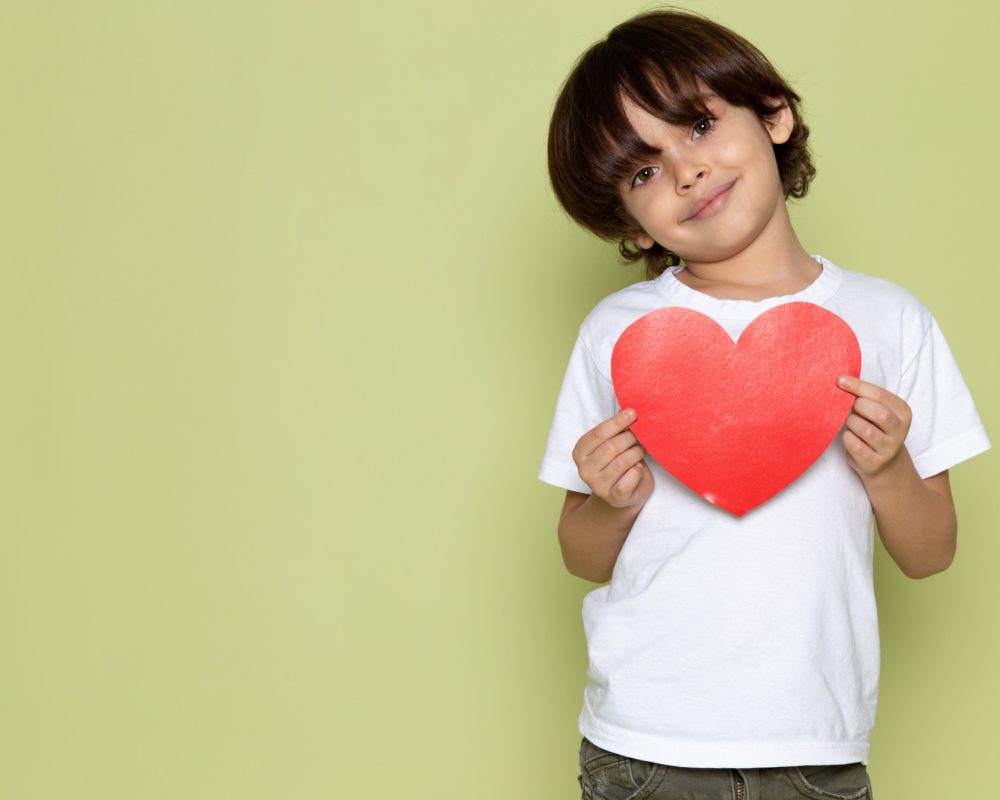 front-view-smiling-cute-boy-white-t-shirt-holding-heart-shape-stone-colored-space